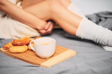 Close up of woman`s legs on the bed. croissants and cup of coffee next to legs.