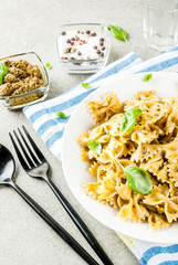 Vegan dinner. Farfalle pasta with pesto sauce and basil leaves on white plate, grey stone background, copy space
