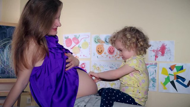 Cute child girl kissing tickle and hug her pregnant woman mom tummy sit on sofa
