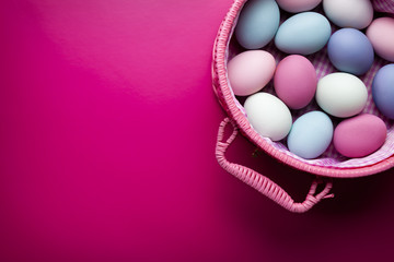 Colored Easter eggs in a basket on pink background