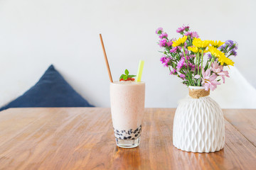 A milkshake with strawberries and jelly, stands on a wooden table on a summer terrace with a flowers in a cafe. Top view with copy space