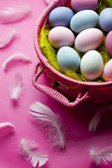 Colored Easter eggs and feathers on pink background