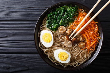 Asian Soba soup with vegetables, mushrooms, egg and sesame seeds close up. Horizontal top view