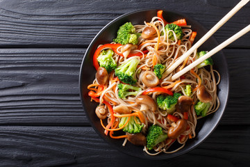 fried soba noodles with mushrooms, broccoli, carrots, peppers closeup on a plate. horizontal top view