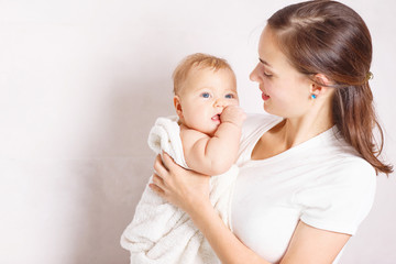 Young woman holding her baby in towel after shower