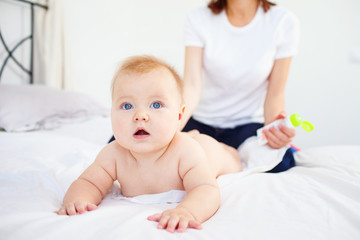 Woman spreading her baby with cream while lying on bed. 