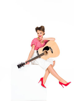 attractive young woman in retro clothing with guitar sitting on cube isolated on white