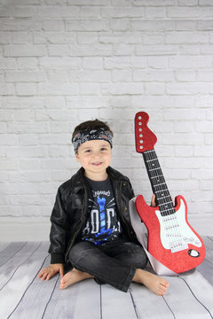 ni&ntilde;o posando con guitarra el&eacute;ctrica de goma eva y ropa rockera
