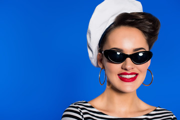portrait of smiling stylish woman in retro clothing and sunglasses isolated on blue
