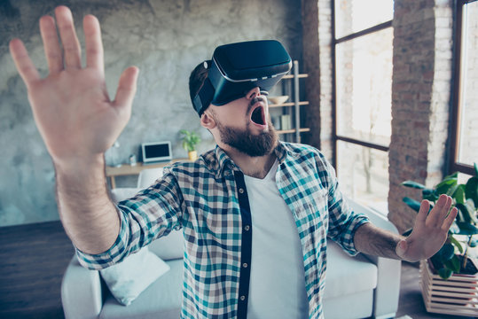 Bearded, shocked, wondered man in shirt with open mouth in motion, getting experience wearing vr goggles headset, watching video, trying to touch something in the air