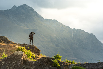 Young male photographer looking at mountain scenery during golden hour sunset in Queenstown, South...