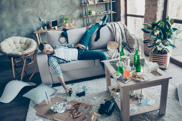 Man, party maker having hangover after stag party, sleeping on sofa, holding bottle of beer with...
