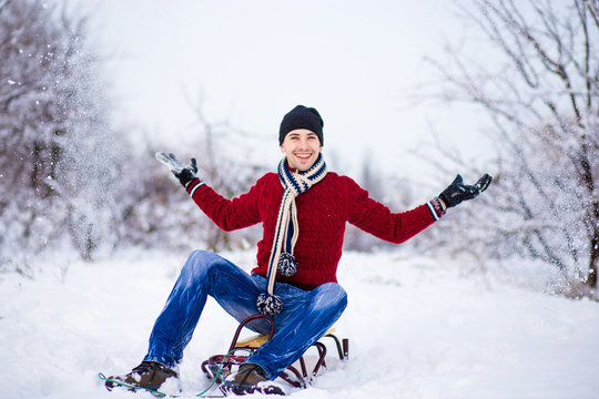 Cheerful young man having fun on a sleigh in snowy weather