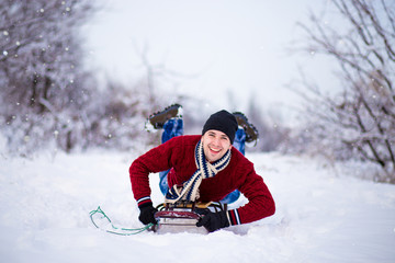 Fototapeta na wymiar Cheerful young man having fun on a sleigh in snowy weather