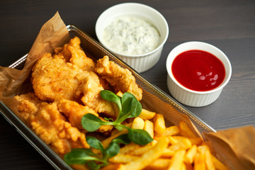 chicken nuggets with french fries and different sauces on wooden board,