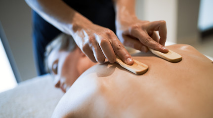 Massage therapist using wooden tool to massage patient