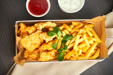 chicken nuggets with french fries and different sauces on wooden board,