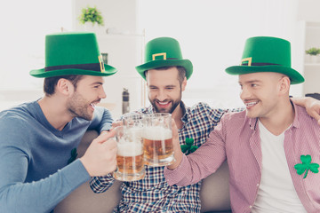 St Patrick's day concept. Close up portrait of laughing, cheerful, positive successful stylish lucky guys with stubble in green hats having glasses with lager in hands, clinking toasting