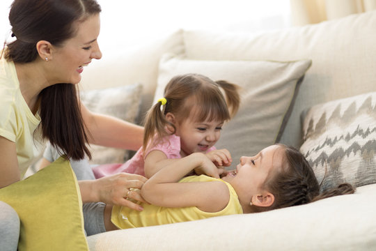 Smiling kids and their mom having a fun pastime together on couch in living room at home