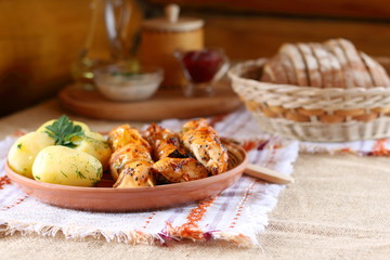 Fried pieces of chicken on skewers and boiled potatoes with greens on a ceramic plate.