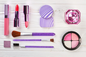 Fototapeta premium Set of female cosmetics, top view. Decorative cosmetics for make up on wooden table. Purple brushes and puff on wooden workplace.