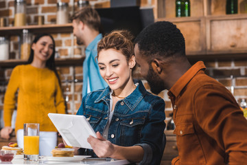 smiling young multiethnic couple using digital tablet at table with juice and pancakes