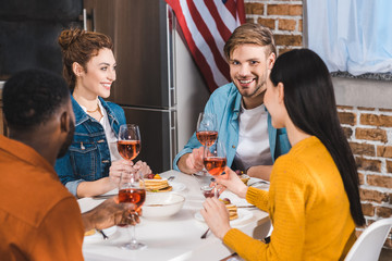 happy young multiethnic friends drinking wine and talking at table