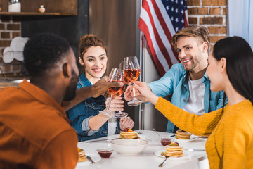 happy young multiethnic friends clinking wine glasses above table