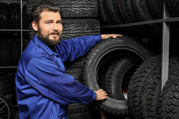 Obraz na płótnie Canvas Male mechanic holding car tire in automobile store