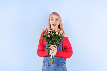 Beautiful young woman with bouquet of roses on color background