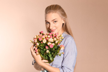 Beautiful young woman with bouquet of roses on color background