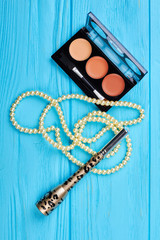 Decorative cosmetics and accessory, top view. Brown eyeshadows palette, white pearl beads and eyeliner. Stylish cosmetics set.