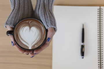Top view female hands holding a cup of hot coffee with heart shape latte art. with copy space.