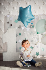 Little boy plays with blue balloons befoe large number one in a cosy room