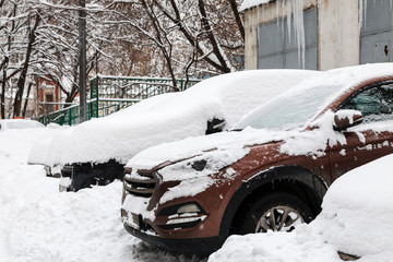 Snow covered cars on a parking near building