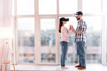 First dance. Full length of sweet innocent satisfied couple posing near window while trying VR glasses and touching each other hands