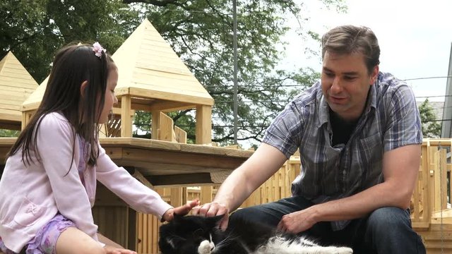 Dad and daughter petting a cat at the playground