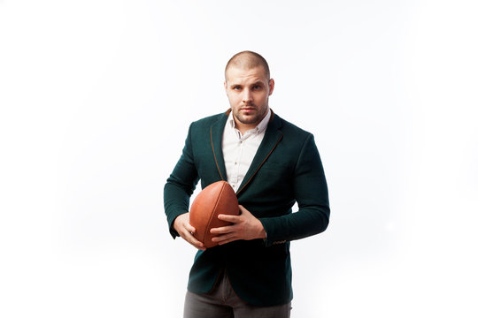 A young bald man in a white shirt, green suit holds a rugby ball in one hand and poses on a white isolated background