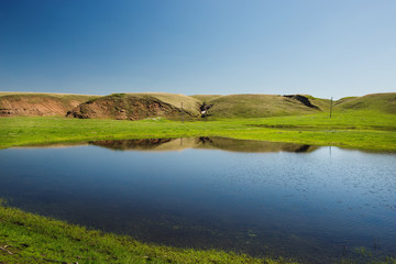 small lake on the background of blue sky and green fields.