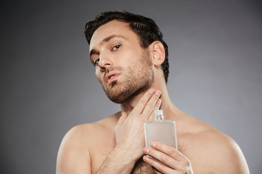 Portrait Of Masculine Sexual Man Putting Perfume Aftershave On His Neck, Isolated Over Gray Background