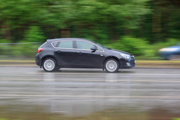 Fototapeta na wymiar Black car is driving on a wet road. Urban life.
