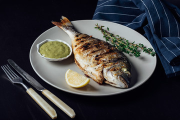 Grilled fish on a plate with lemon sauce and thyme