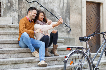 Young smiling couple using mobile phone while sitting on the stairs.
