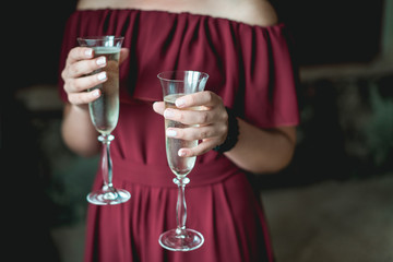 girl in a pomegranate dress and with french manicure holding in her hands two glasses with champagne