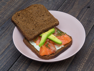 Sandwich with salmon, avocado and black bread on a plate