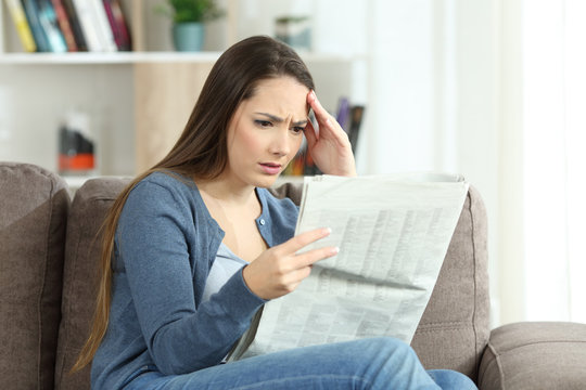 Concerned woman reading a newspaper on a sofa