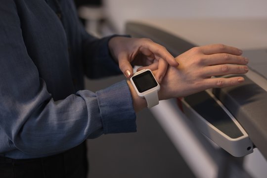 Mid section of female executive using smartwatch on treadmill