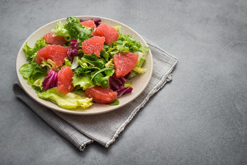 Fresh mix salad with lettuce, green arugula and sliced grapefruit in a plate