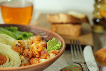 Clay plate with prawns and pasta on the table, next to bread, tea and cutlery