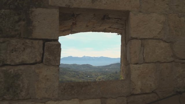 Small breach in the wall of a medieval fortress that shows mountains in the distance, in Abruzzo.